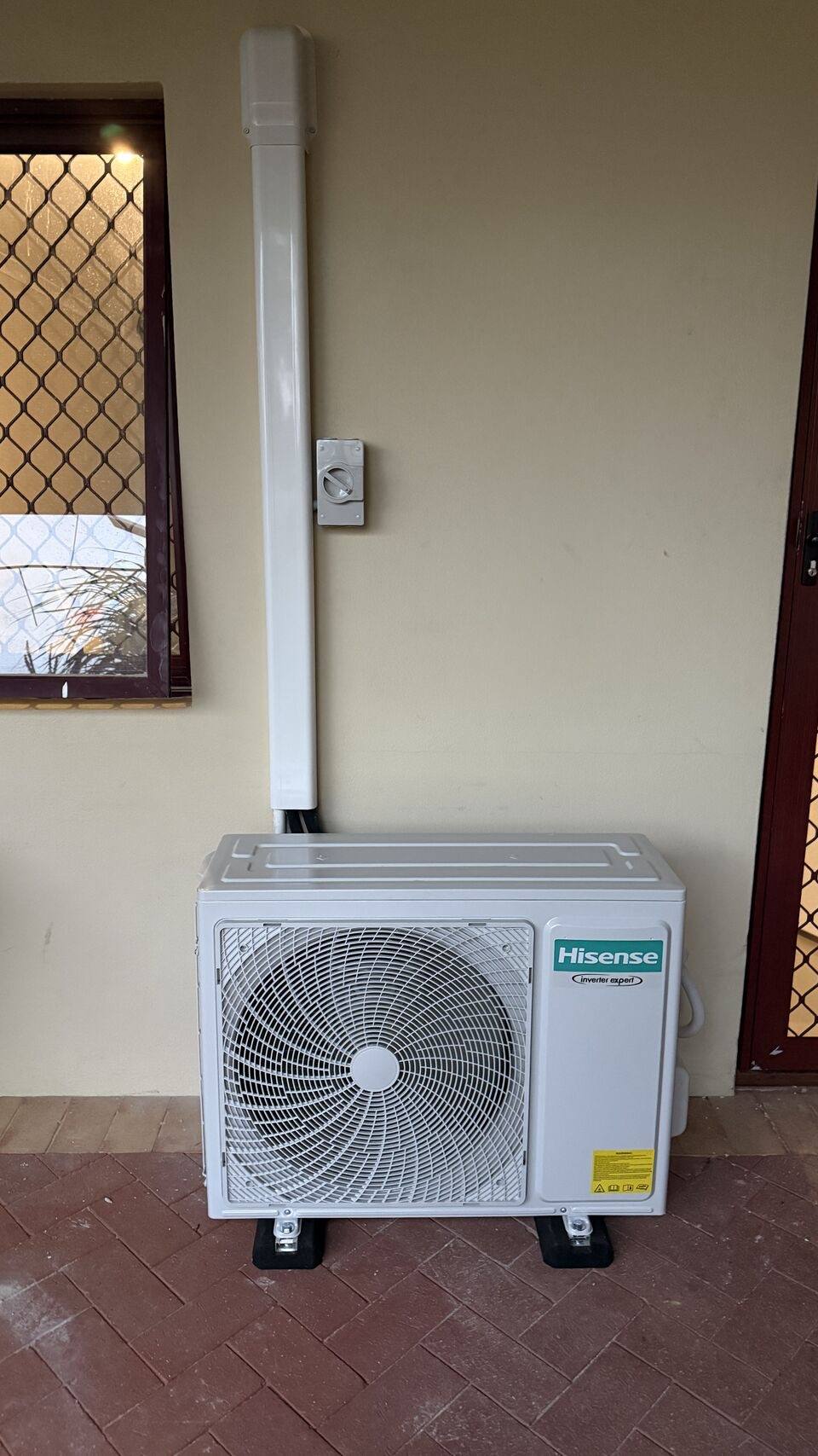 Condenser on ground feet with white conduit running up the wall